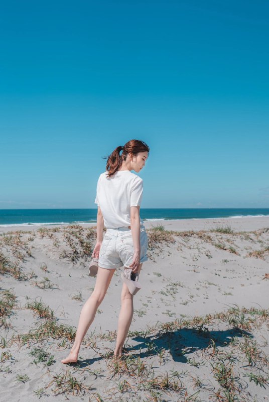 穿着白色衬衫和短裤的女人在海滩上散步